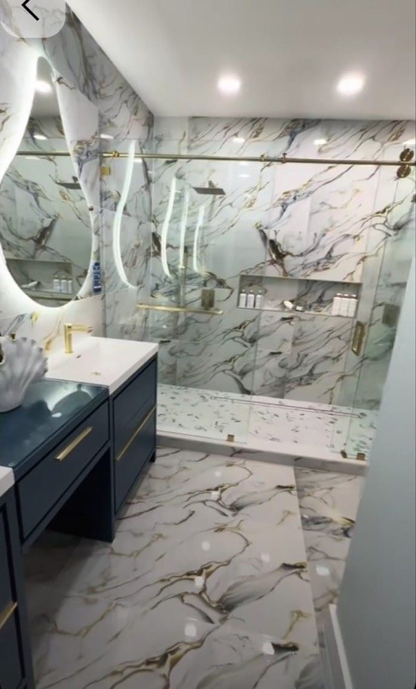 Yenilenmiş banyo: mermer desenli duvar ve zemin, camlı duş alanı, lacivert lavabo dolabı