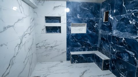 Beyaz mermer desenli duvarlar, lacivert mermer duş nişi ve oturma bankı olan bitmiş banyo